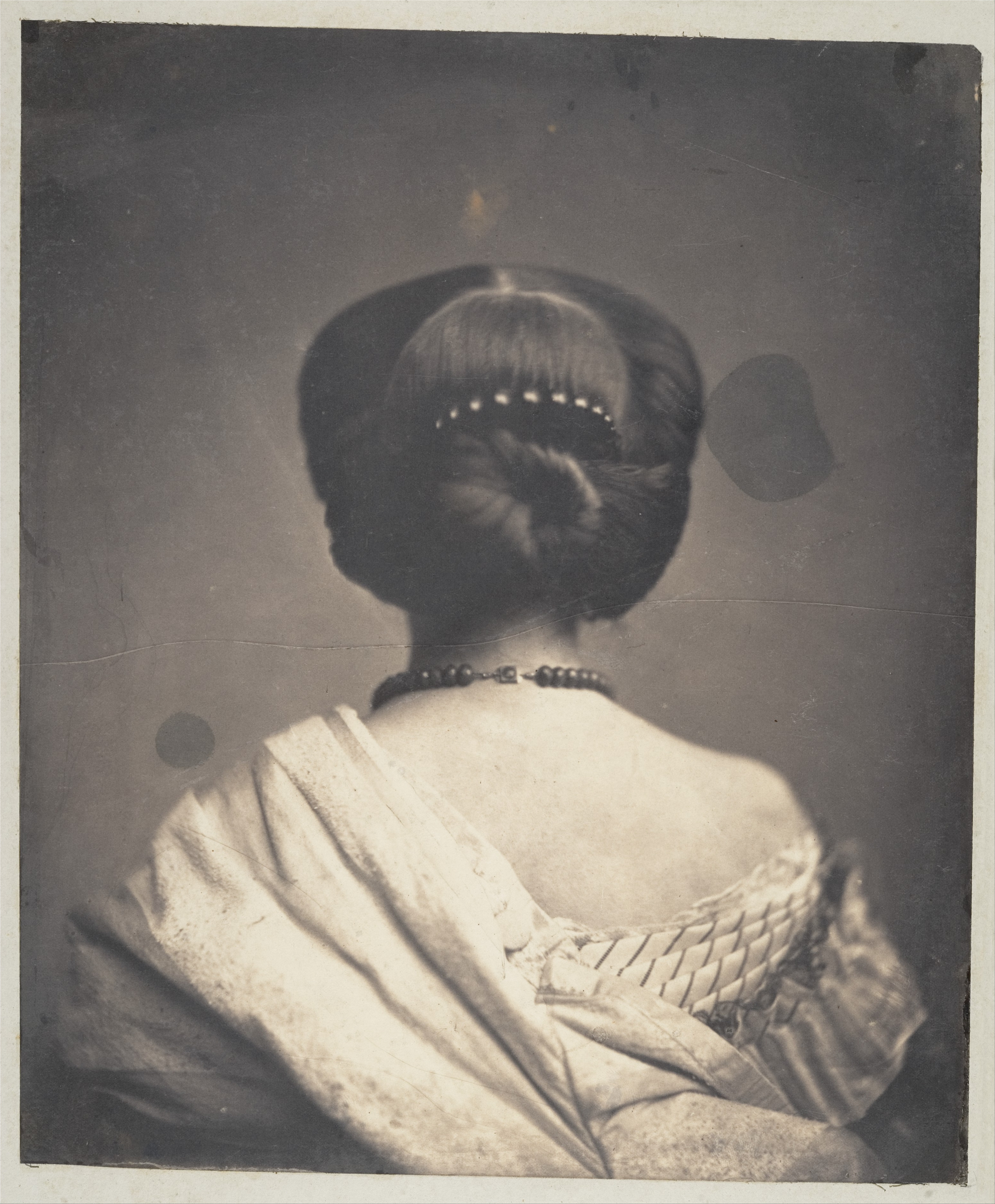 Historic black and white picture of the back of a woman’s head with a decorative curved comb nestled in her updo hairstyle.